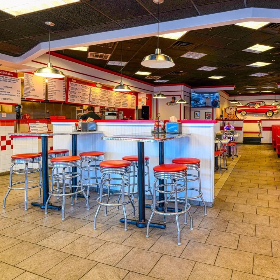 Interior of The Burger Shop, a fast-food restaurant with red and white decor, bar stools, and menu boards.