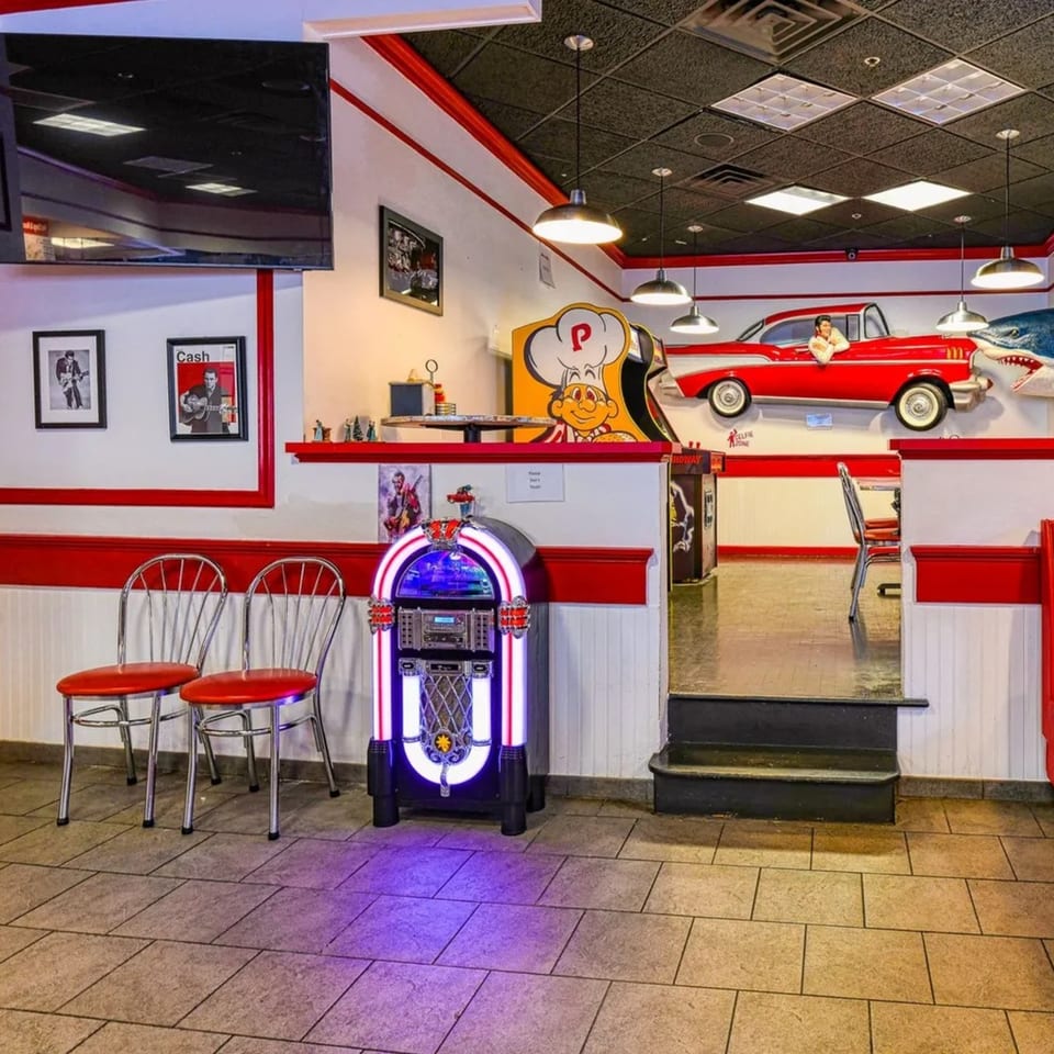 Retro-themed fast-food diner interior with a jukebox, red booths, and a classic car wall decoration.