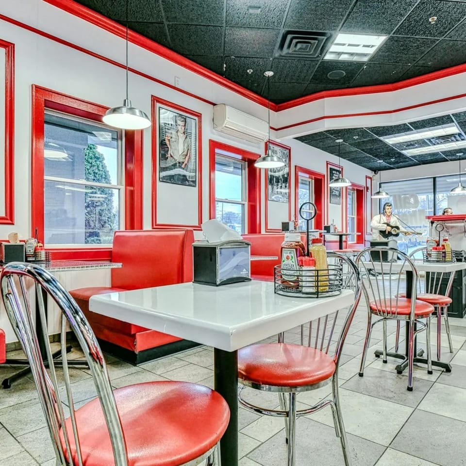Retro diner interior with red booths, chrome chairs, white tables, and an Elvis Presley cutout.