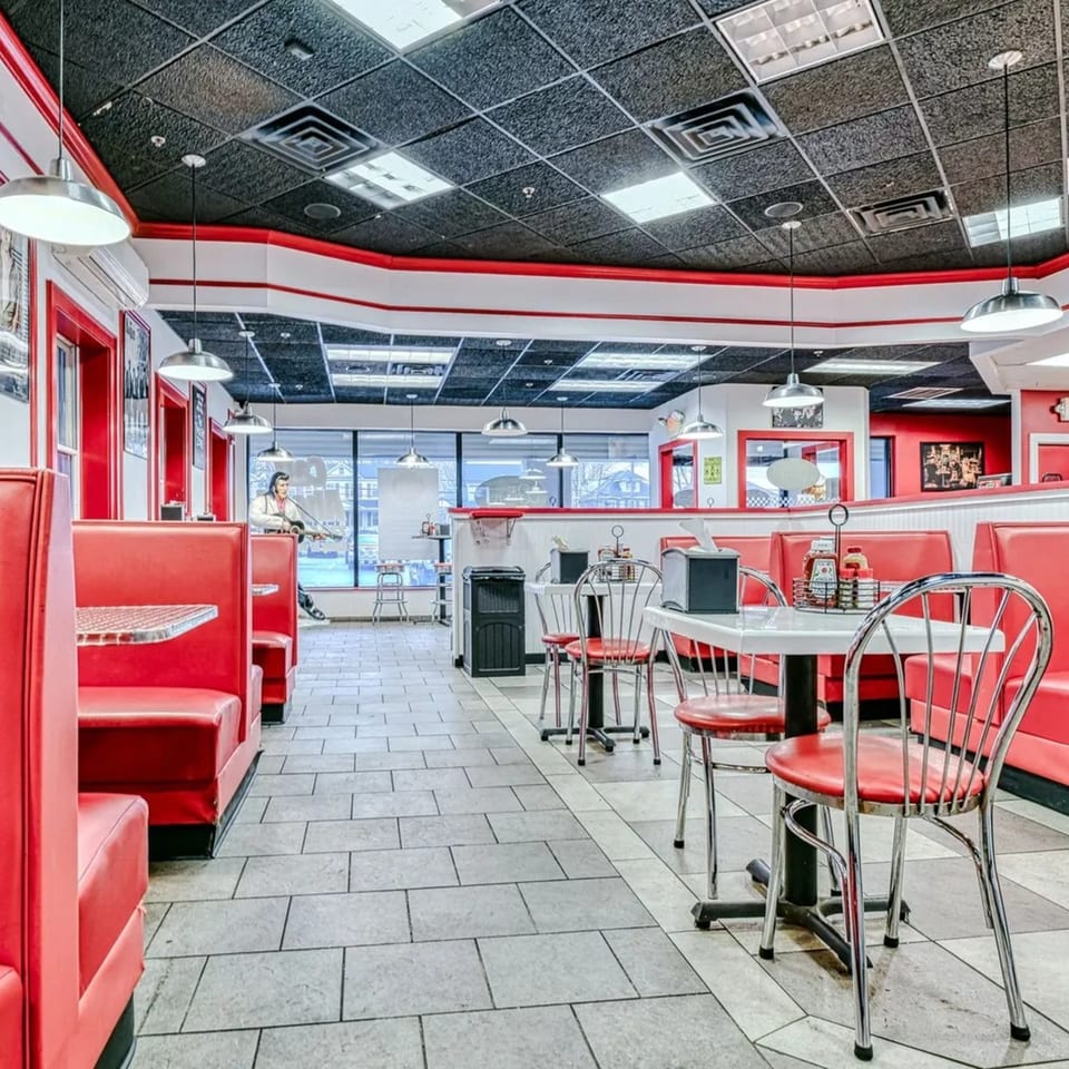 Interior of The Burger Shop, a fast-food restaurant with red booths, chrome chairs, and tiled floors.