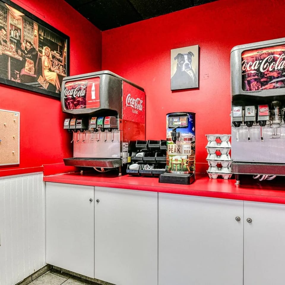 Fast-food drink station with red walls, Coca-Cola dispensers, and a Gold Peak Iced Tea machine.