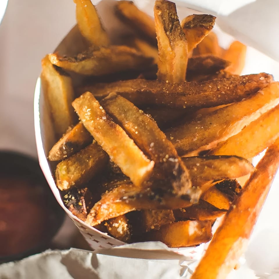 Close-up of golden-brown, salted french fries in a paper cone from The Burger Shop.