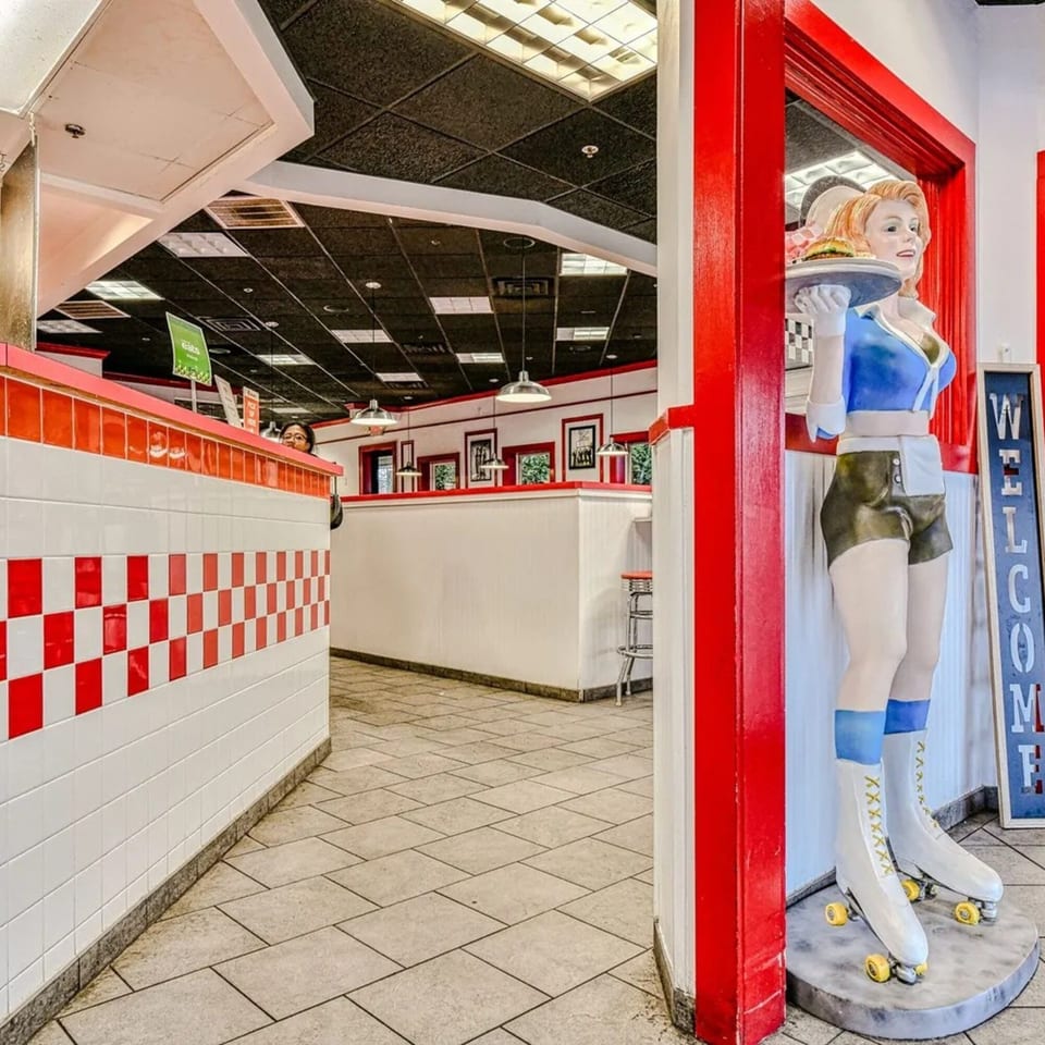 A diner-style restaurant interior with red and white checkered walls and a retro waitress statue.