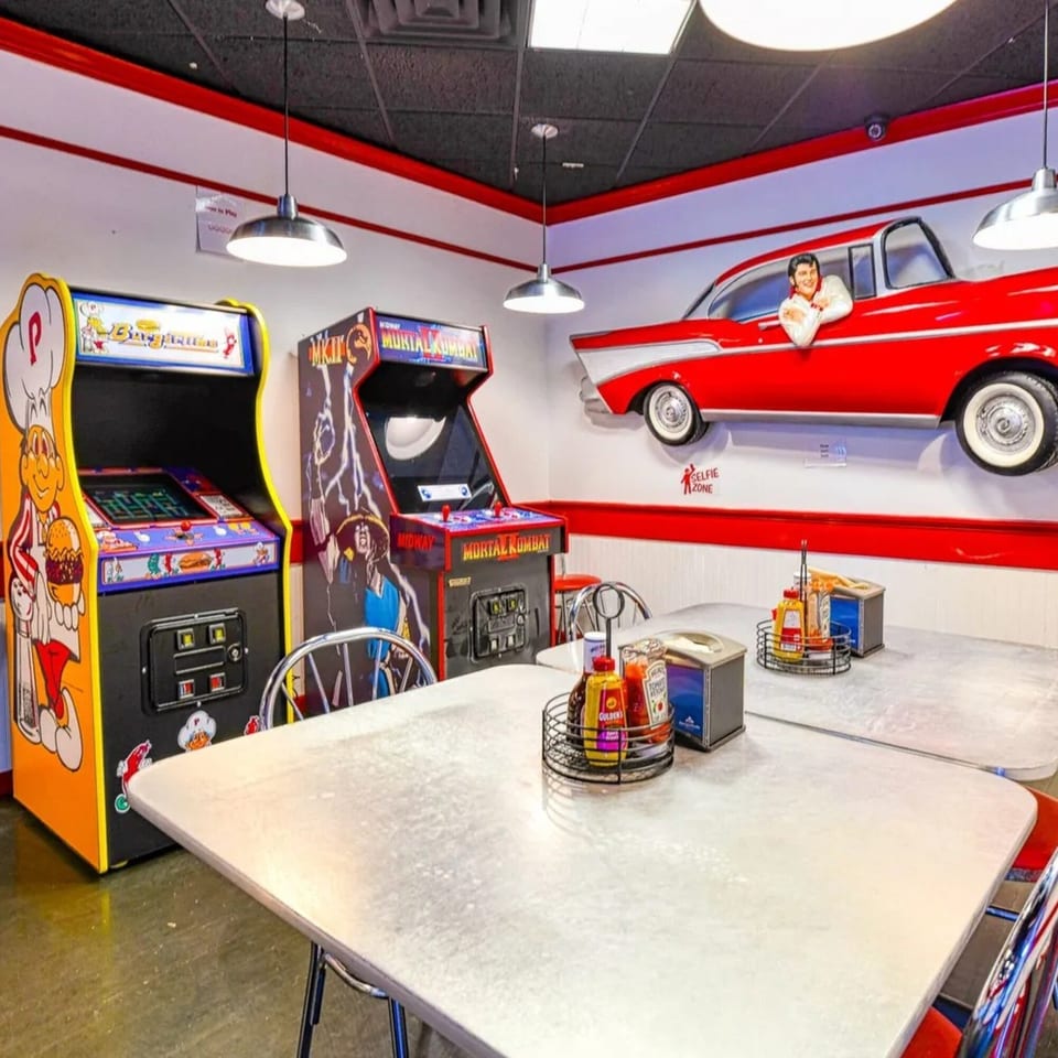 Retro-themed diner interior with arcade games, booths, and a red classic car wall decoration.