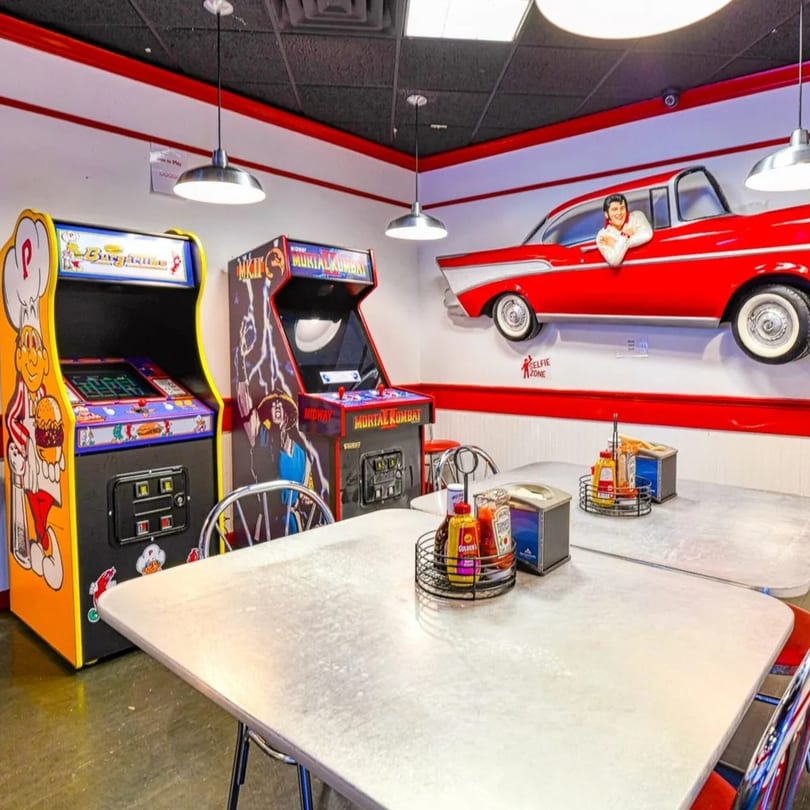Retro-themed diner interior with arcade games, booths, and a red classic car wall decoration.