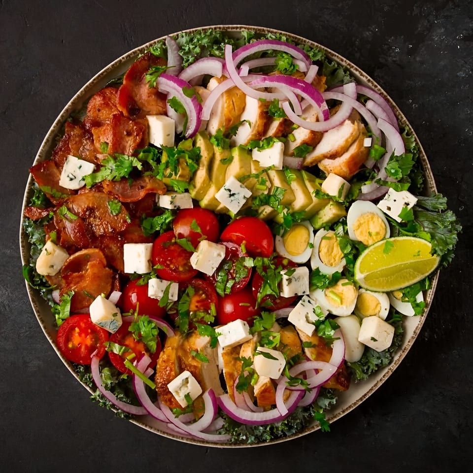 A vibrant Cobb salad with chicken, bacon, avocado, tomatoes, eggs, and blue cheese on kale.