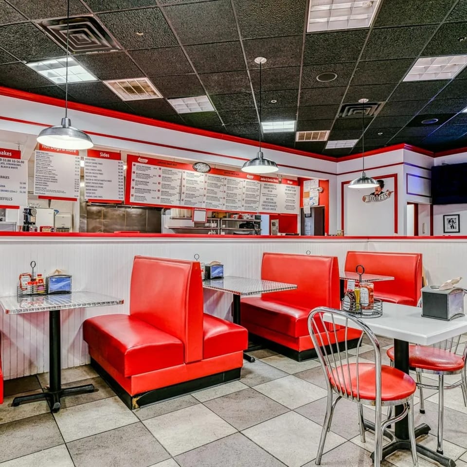 Interior of The Burger Shop with red booths, checkered floor, and menu boards above the counter.