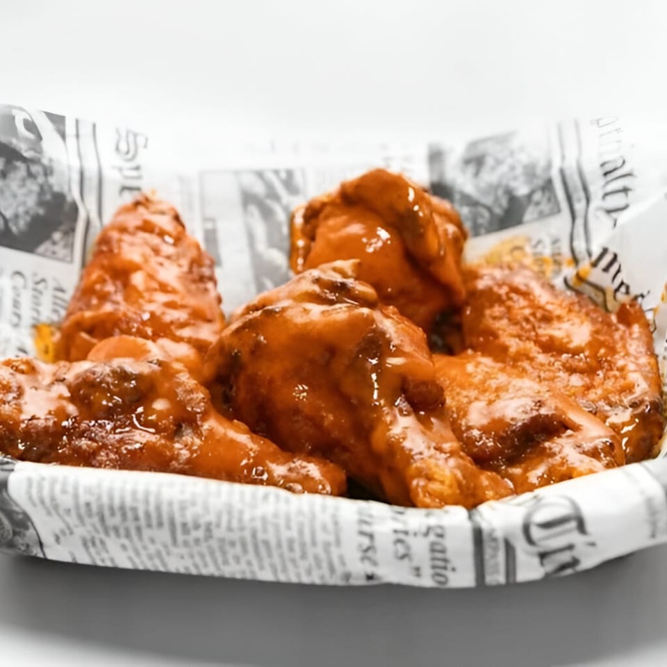 The Burger Shop's buffalo wings, coated in a glossy orange sauce, served in a newspaper-lined basket.
