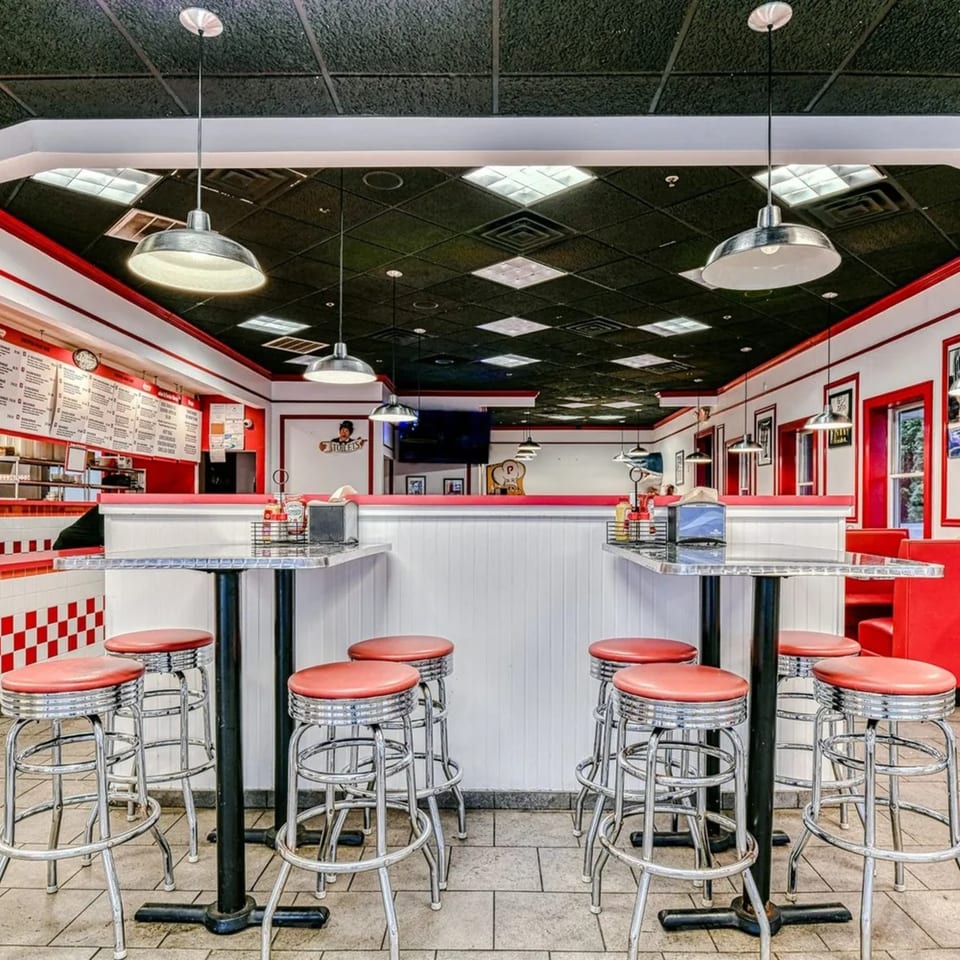 The Burger Shop interior with red and white checkered walls, red stools, and silver tables.