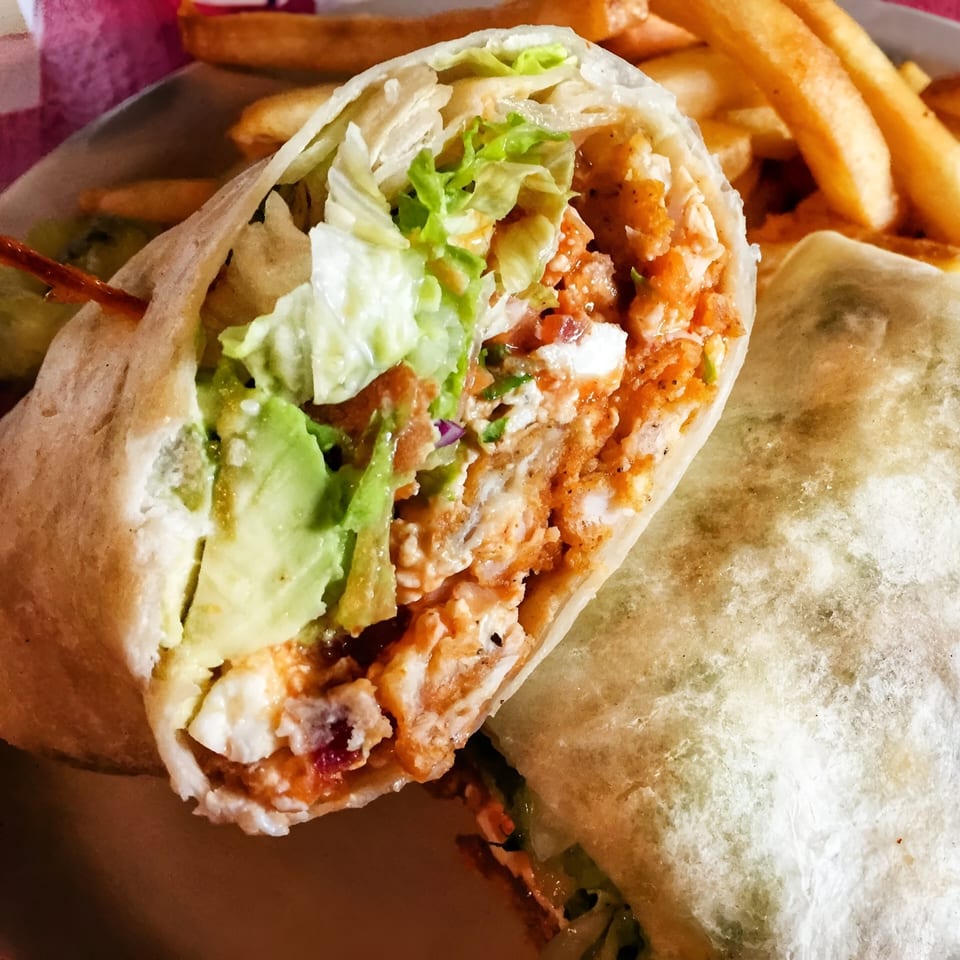 A buffalo chicken wrap with avocado, lettuce, and cheese, served with a side of fries.
