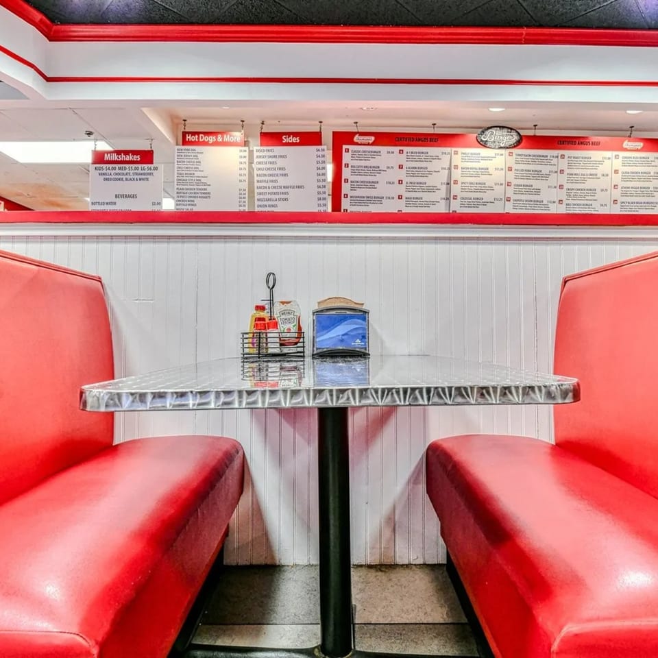 Red booths and a shiny table with condiments in a fast-food restaurant, with menu boards above.