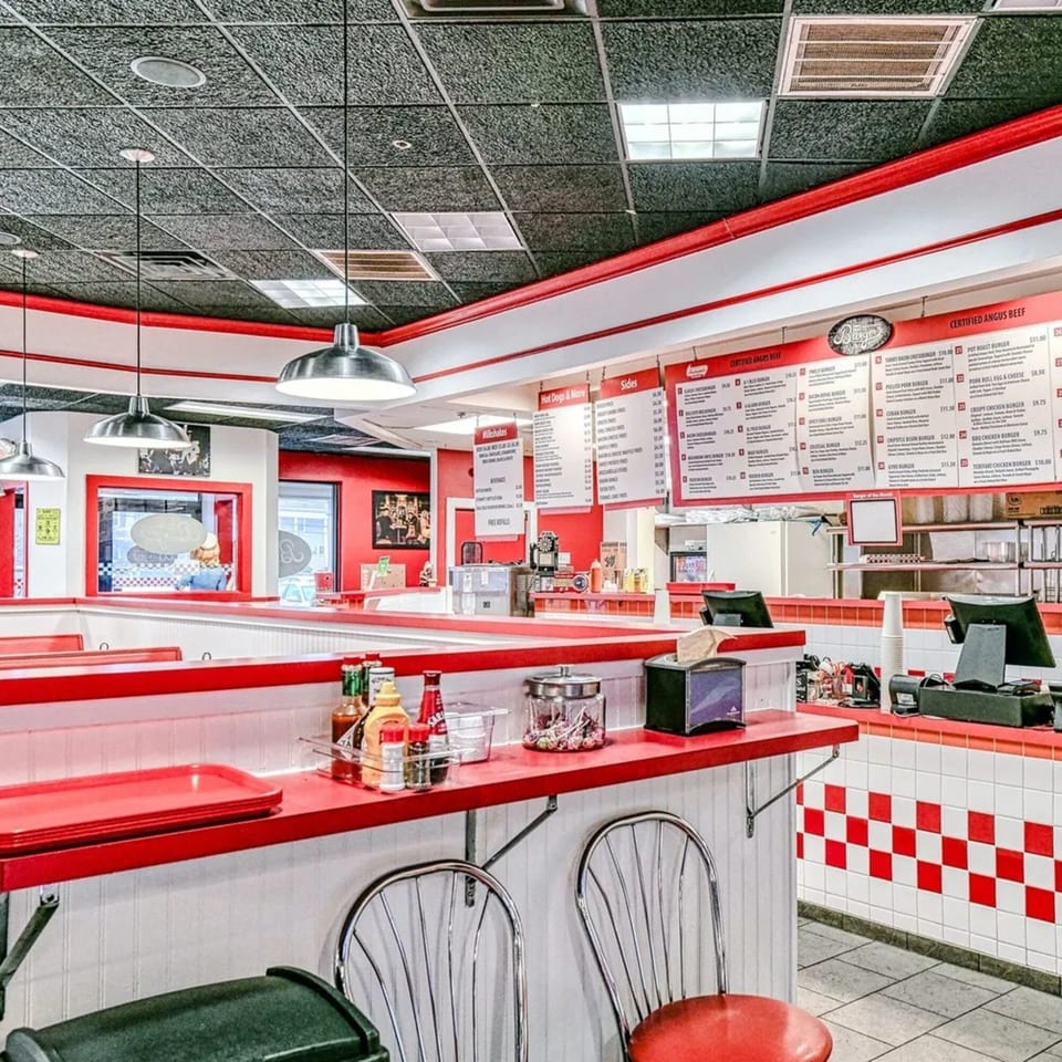 The Burger Shop's fast-food interior features red and white decor, menu boards, and counter seating.
