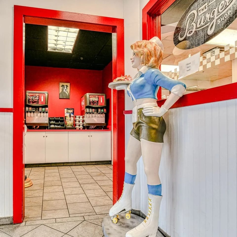 A retro roller-skating waitress statue holding a burger tray, with soda fountains in the background.