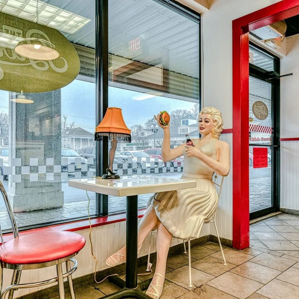 A Marilyn Monroe mannequin holds a burger and soda at a table inside The Burger Shop.